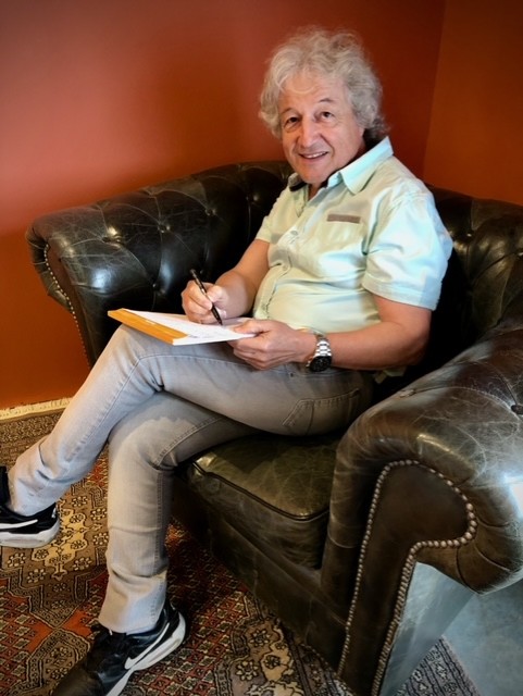Tony Sampieri écrivant, assis dans un fauteuil en studio